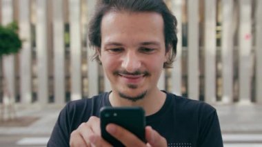 Genç adam dışarıda telefon kullanıyor.