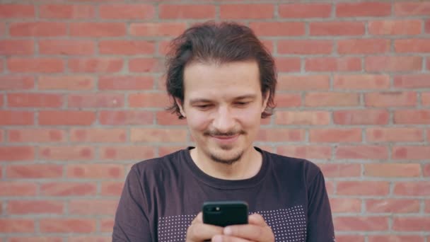 Jonge Man met behulp van een telefoon tegen een bakstenen muur achtergrond — Stockvideo