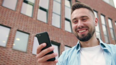 Sakallı bir tuğla bina karşı bir telefonu kullanarak