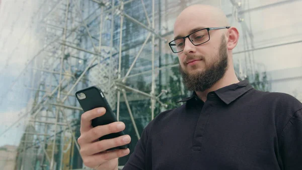 Homem com barba usando óculos usando um telefone na cidade — Fotografia de Stock