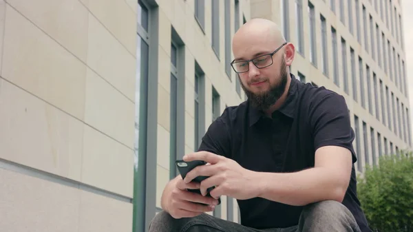 Человек в очках с бородой, использующий телефон в городе — стоковое фото