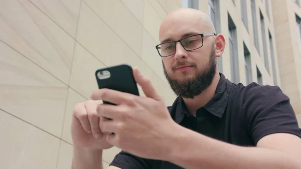 Férfi szakáll, szemüveg segítségével a telefon, a város — Stock Fotó