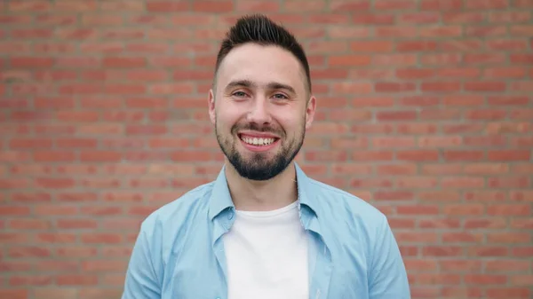 Man met baard glimlachend tegen een bakstenen muur — Stockfoto