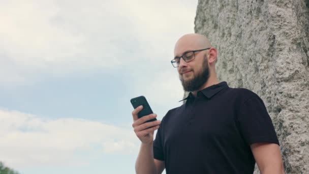 Homem com barba usando óculos usando um telefone ao ar livre — Vídeo de Stock