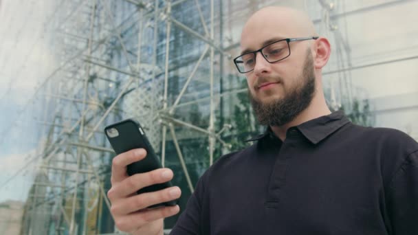 Hombre con barba usando gafas usando un teléfono en la ciudad — Vídeo de stock