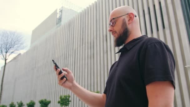 Człowieka z brodą, w okularach, korzystając z telefonu w mieście — Wideo stockowe