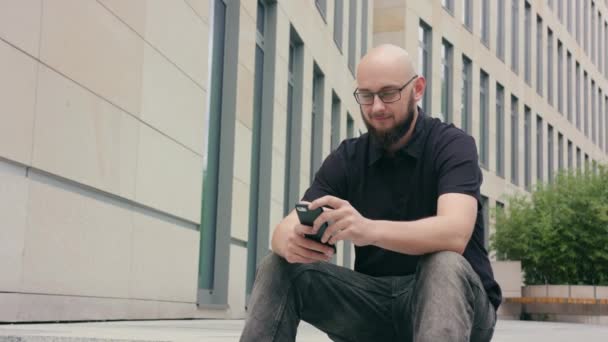 Férfi szakáll, szemüveg segítségével a telefon, a város — Stock videók
