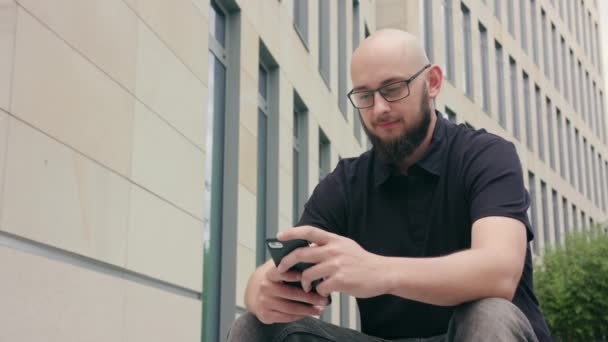 Człowieka z brodą, w okularach, korzystając z telefonu w mieście — Wideo stockowe