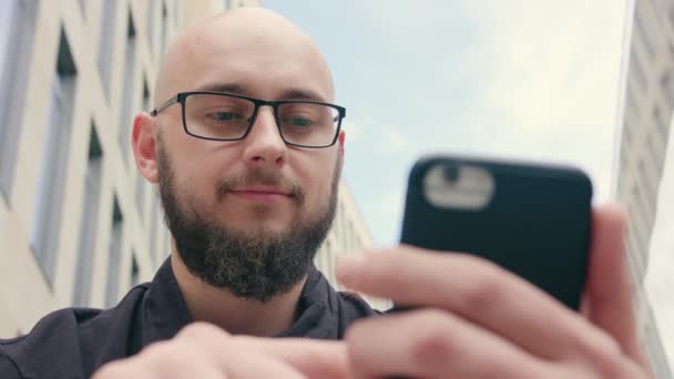 Człowieka z brodą, w okularach, korzystając z telefonu w mieście — Wideo stockowe