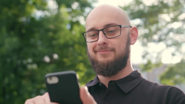 Férfi szakáll, szemüveg segítségével a telefon, a város — Stock videók