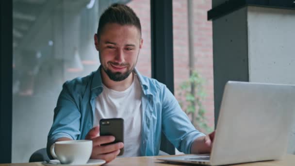 Een jonge Man met behulp van een Computer en een telefoon binnenshuis — Stockvideo