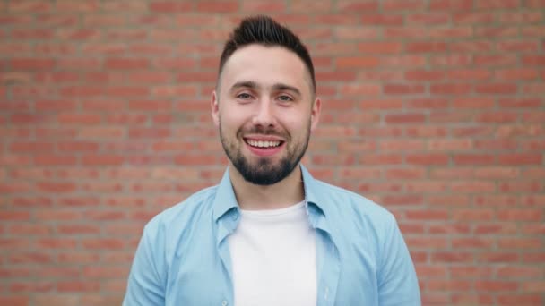 Hombre con barba sonriendo contra una pared de ladrillo — Vídeos de Stock