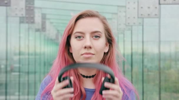 Mulher com cabelo rosa colocando em fones de ouvido na cidade — Vídeo de Stock