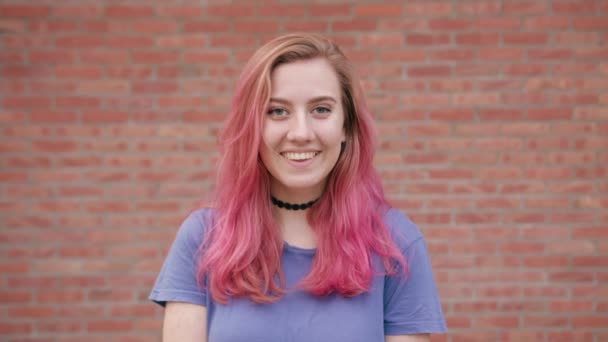 Mulher sorridente feliz com cabelo rosa contra a parede de tijolo — Vídeo de Stock