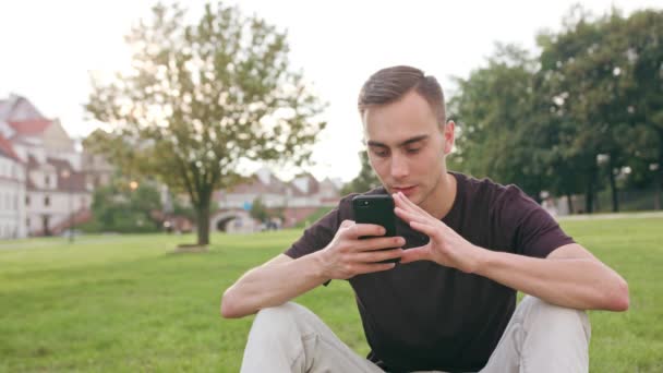 公園で携帯電話を使用して若い男 ミディアム ショット ソフト フォーカス — ストック動画