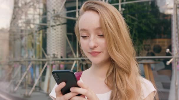 Νεαρή κοκκινομάλλα κοπέλα χρησιμοποιώντας ένα τηλέφωνο στην πόλη — Αρχείο Βίντεο