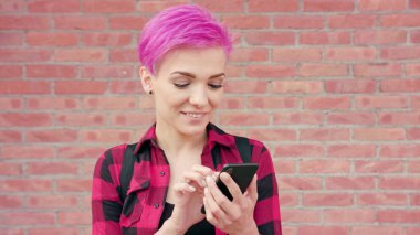 Duvara karşı bir telefonu kullanarak pembe saçlı kadın