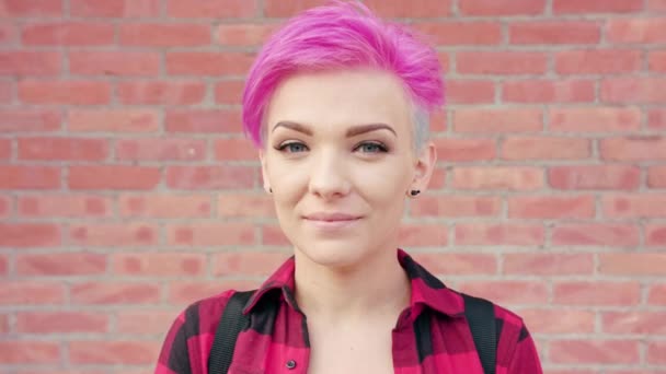 Mulher sorridente feliz com cabelo rosa contra a parede de tijolo — Vídeo de Stock