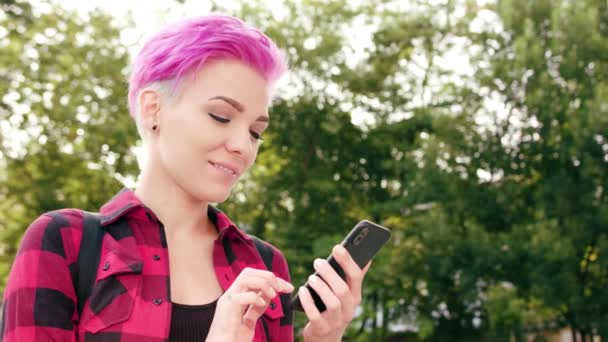 Mujer con el pelo corto rosa usando un teléfono en la ciudad — Vídeos de Stock