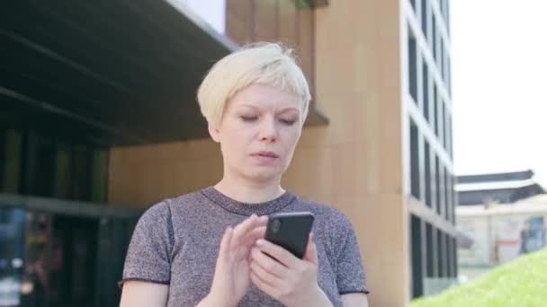 Ung blond Lady promenader och använder en telefon i stan — Stockvideo