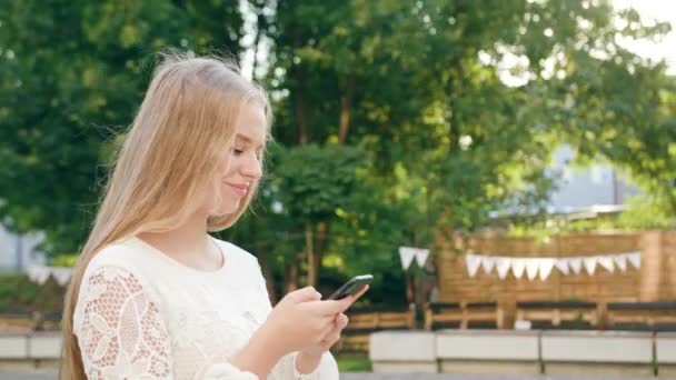 Ung blond Lady promenader och använder en telefon i stan — Stockvideo