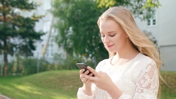 Joven rubia dama caminando y usando un teléfono en la ciudad — Vídeos de Stock