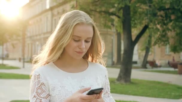Mladá blondýnka dáma chůzi a používání telefonu ve městě — Stock video