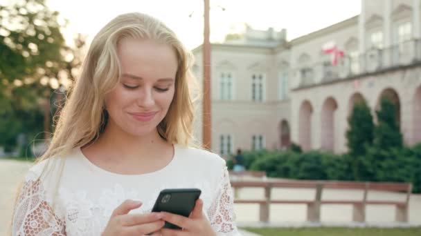 Ung blond Lady promenader och använder en telefon i stan — Stockvideo