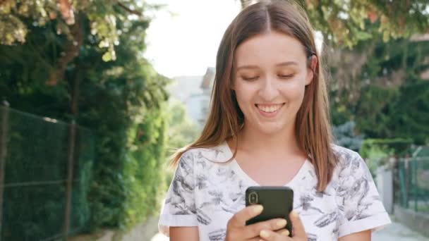 Junge Frau benutzt Handy in der Stadt beim Gehen — Stockvideo