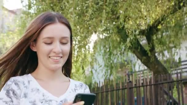 Junge Frau benutzt Handy in der Stadt beim Gehen — Stockvideo