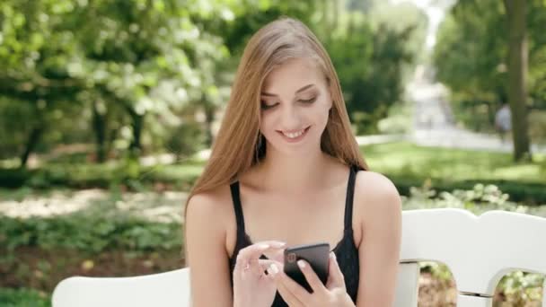 Junge Frau sitzt auf der Bank und benutzt ein Telefon — Stockvideo