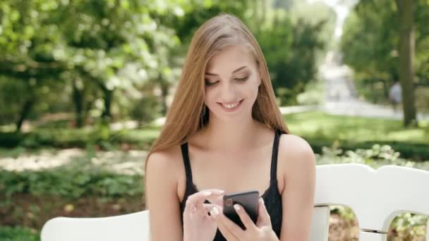 Jovencita sentada en el banco y usando un teléfono — Vídeo de stock