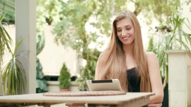 Jovencita usando una tableta en la ciudad sentada a la mesa — Vídeo de stock