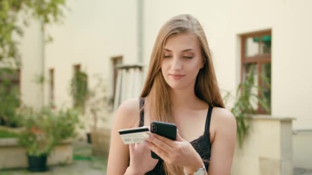 Jovencita usando un teléfono y sosteniendo tarjeta de crédito — Vídeos de Stock