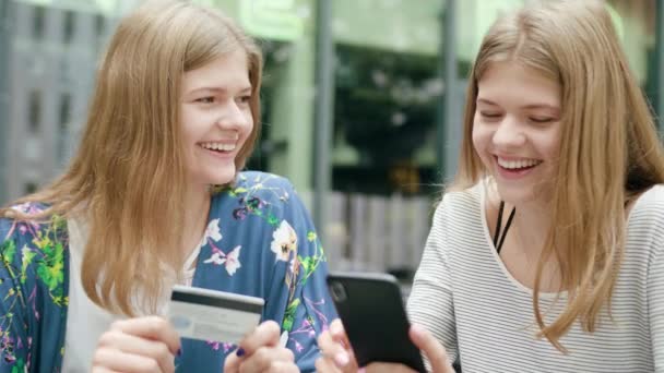 Señoras jóvenes usando un teléfono y la celebración de tarjeta de crédito — Vídeos de Stock