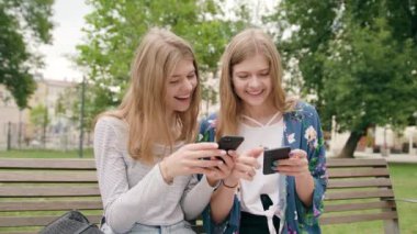 Bankta oturan ve şehirde bir telefonu kullanarak çekici genç bayanlar. Orta atış