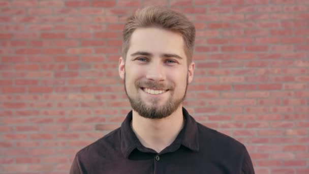 Heureux homme souriant avec barbe contre un mur de briques — Video