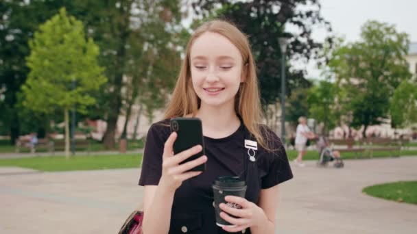 Ung rödhårig dam promenader och använder en telefon i stan — Stockvideo