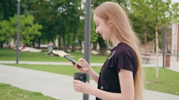 Ung rödhårig dam promenader och använder en telefon i stan — Stockvideo