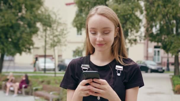 Jonge roodharige dame met behulp van een telefoon in de stad — Stockvideo