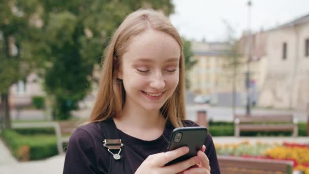 Νεαρή κοκκινομάλλα κοπέλα χρησιμοποιώντας ένα τηλέφωνο στην πόλη — Αρχείο Βίντεο