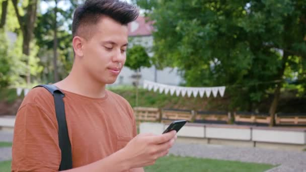 Молодой человек ходит и пользуется телефоном в городе — стоковое видео