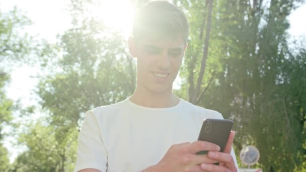 街で携帯電話を使用して白いシャツを着て魅力的な若い男 クローズ アップ ショット ソフト フォーカス レンズ フレア — ストック動画