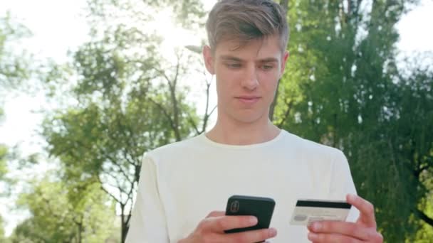 Νεαρός άνδρας χρησιμοποιώντας ένα τηλέφωνο και μια πιστωτική κάρτα στην πόλη — Αρχείο Βίντεο