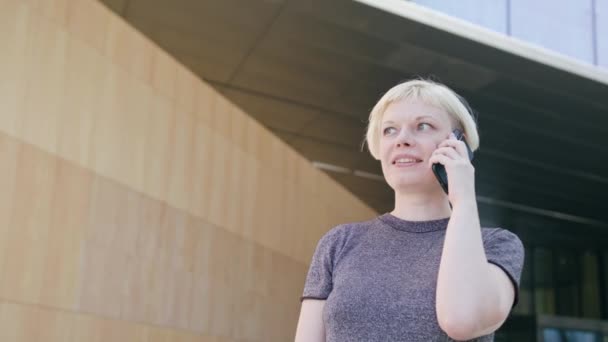 Молодая блондинка говорит по телефону в городе — стоковое видео