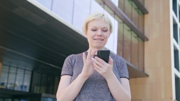 Jonge Blonde dame met behulp van een telefoon in de stad — Stockvideo