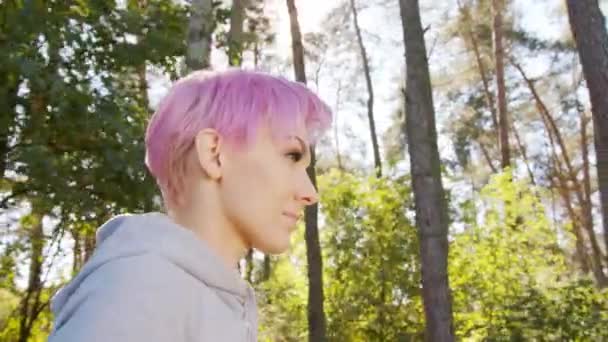 Jeune femme aux cheveux roses marchant dans la forêt — Video