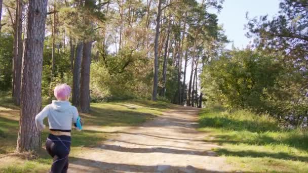 Ung dam med rosa hår jogga i skogen — Stockvideo