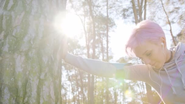 Jeune femme aux cheveux roses s'étendant dans la forêt — Video