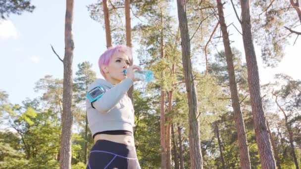 Junge Frau mit rosa Haaren joggt im Wald — Stockvideo